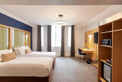 a hotel room with two beds and a desk at Thistle London Park Lane in London