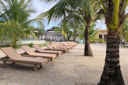 a row of chaise lounges on a beach with palm trees at Maruti Beach Villas in Nusa Penida