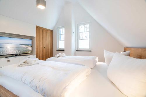 a white bedroom with two beds and a flat screen tv at Ferienhaus Baltic Huus in Zirchow