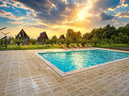 a pool with chairs and a sunset in the background at Zholovani Cottages in Lagodekhi