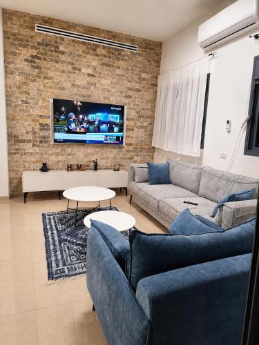 a living room with a couch and a tv on a brick wall at הפינה של פנינה במושבה - דירה משפחתית מהממת in Migdal
