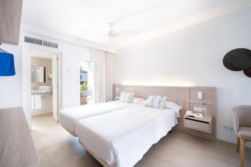 a white bedroom with a large bed and a chair at Serenity Apartments in Port d'Alcudia