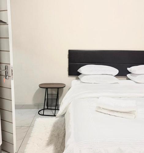 a bedroom with a bed with white sheets and a stool at Ekhaya Loft in Mbabane