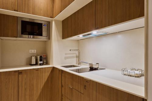 a kitchen with wooden cabinets and a sink and a microwave at Glinter Barrio de las Letras - Apartments in Madrid