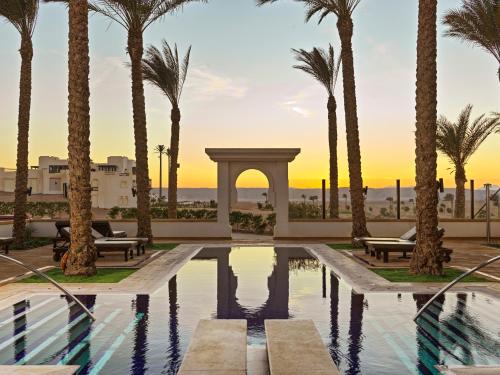 a resort pool with palm trees and a sunset at Ancient Sands Golf Resort and Residences in Hurghada
