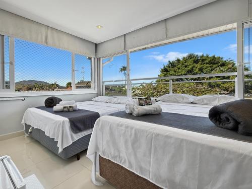 two beds in a room with large windows at AC - Piscina - 1 Suite com banheiro - 200m do mar in Guarujá
