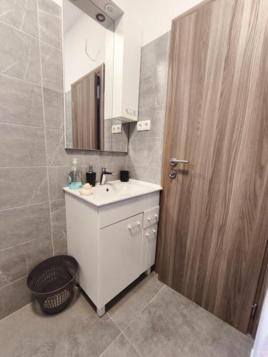 a bathroom with a white sink and a wooden door at Ora Apartment in Kastel Sucurac