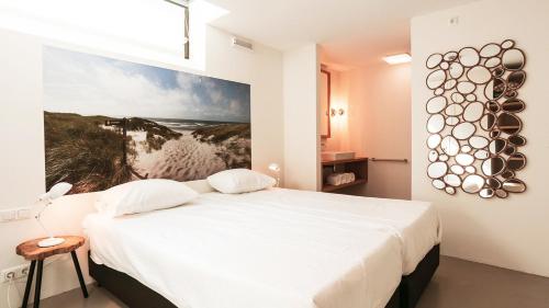 a bedroom with a white bed and a painting on the wall at Dutchen Park Duynzoom in De Koog