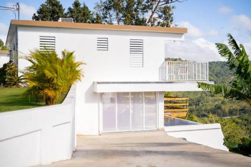 a white house with a balcony and a driveway at Casa Brisa with Heated Pool Mountain View & River in Las Marias