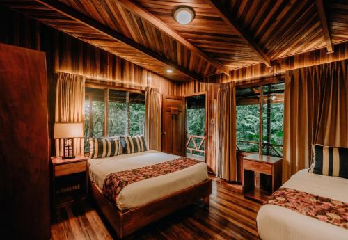 two beds in a room with wooden walls and windows at Jaguarundi Jungle Lodge - Monteverde in Monteverde Costa Rica
