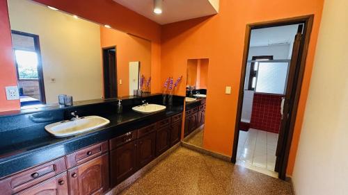 a bathroom with two sinks and an orange wall at Fina residencia con chimenea en Lambaré in Asunción