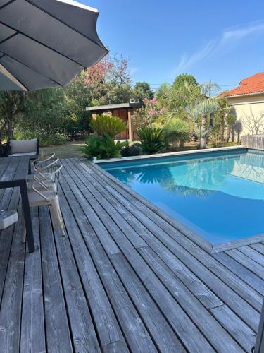 a swimming pool with a wooden deck and an umbrella at Les mimosas in Tosse