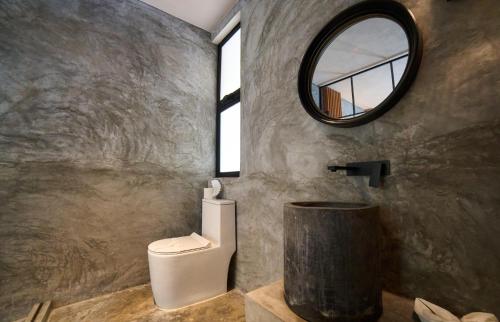 a bathroom with a toilet and a round mirror at Casa del Viento by ÓOL Hotels in Holbox Island
