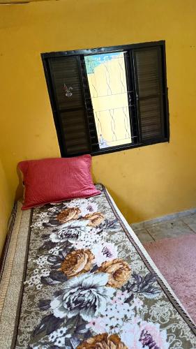 a bed with a red pillow and a window at Casa in Barretos