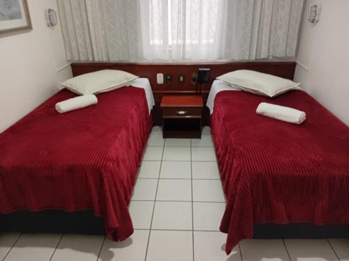 two beds in a hotel room with red sheets at Eduardos Hotel in Rio do Sul
