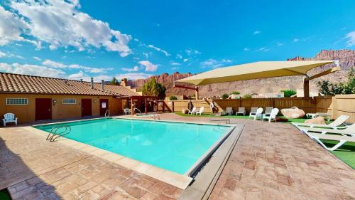 a swimming pool with a patio with chairs and an umbrella at Desert Hideaway #C2 in Moab
