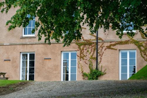 a brick building with two windows and a tree at Glebe House in Sion Mills
