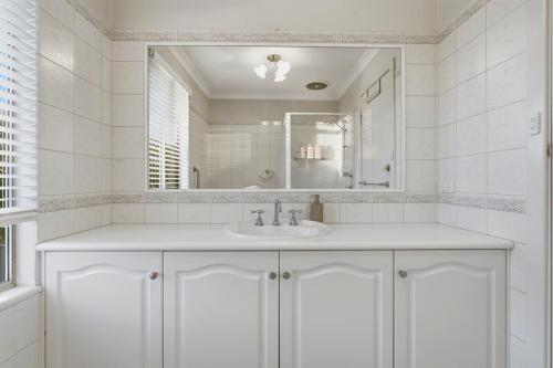 a white bathroom with a sink and a mirror at Mediterranean Beachside retreat with a pool in Broadwater