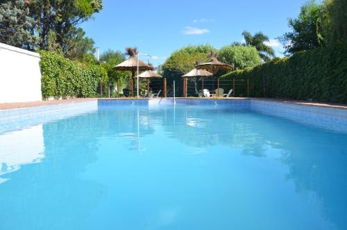 a swimming pool with blue water and umbrellas at Hotel Carmen de Areco in Carmen de Areco