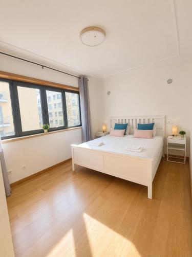 a white bedroom with a large white bed with blue pillows at Bom dia Parque Nações LisboaZ in Lisbon