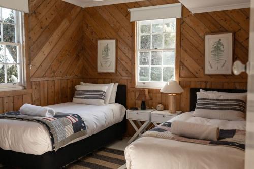 two beds in a room with wooden walls and windows at White Shell Cottage - Woodfire & Beachfront in Falmouth