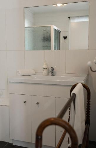 a white bathroom with a sink and a mirror at White Shell Cottage - Woodfire & Beachfront in Falmouth