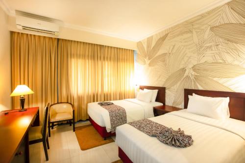 a hotel room with two beds and a desk at MMUGM Hotel in Yogyakarta