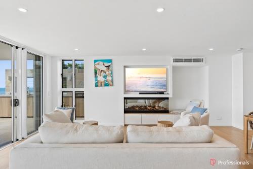 a white living room with a couch and a tv at Waters Edge On Wattle, Absolute Beachfront Luxury in Yeppoon