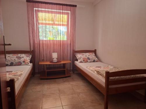 two beds in a room with a window and a table at Sandra Apartmani 1 in Zaostrog