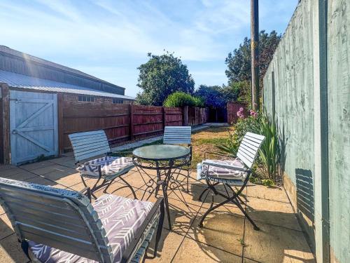 a patio with three chairs and a table and a fence at Penny Cottage in Heacham