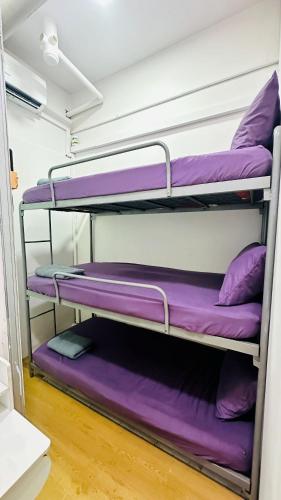 three bunk beds in a room with purple pillows at Bidara Guest House in Kampong Sungai Baru Tengah