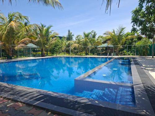 a large blue swimming pool with palm trees in the background at Chill Hutz in Vedakudiyiruppu
