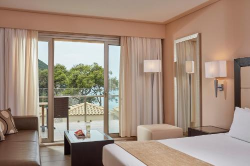 a hotel room with a bed and a large window at Atlantica Grand Mediterraneo Resort - Adults Only in Kompítsion