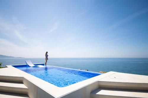 a woman standing on the edge of a swimming pool overlooking the ocean at eureka awaji 絶景インフィニティプール x 露天温水ジャグジー付きヴィラ in Sumoto