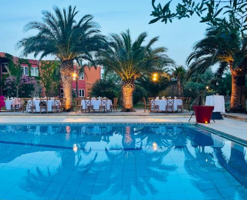 a swimming pool with palm trees and tables at Tropic Hôtel in Rivesaltes