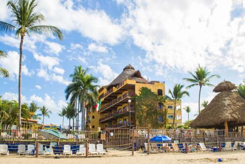 a hotel on the beach with chairs and palm trees at Cabañas del Capitan in Rincon de Guayabitos
