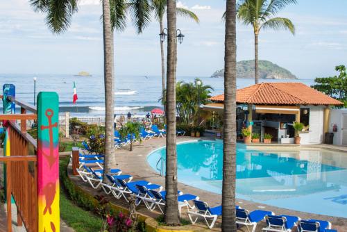 a resort with a pool and palm trees and the ocean at Cabañas del Capitan in Rincon de Guayabitos