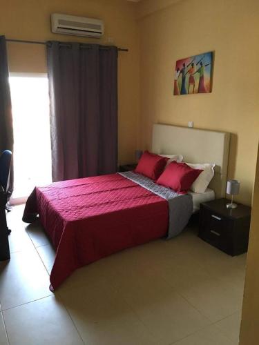 a bedroom with a large bed with red sheets and a window at Hotel Gabu Karsa in Gabú