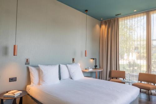 ein Schlafzimmer mit einem weißen Bett und einem großen Fenster in der Unterkunft Pattùs Hôtel in Saint Aubin Sauges