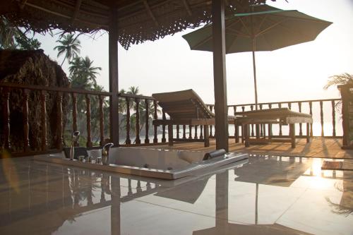 a bath tub on a patio with chairs and an umbrella at The Cape Goa in Cabo de Rama