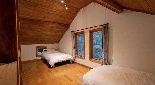 two beds in a room with wooden ceilings and windows at Daruma in Nasu