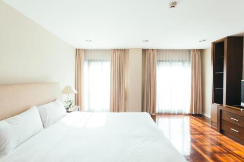 a bedroom with a large white bed and windows at Thomson Residence Hotel in Bangkok