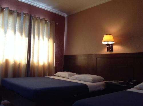 a bedroom with two beds and a lamp and a window at Miami Inn in Cagayan de Oro