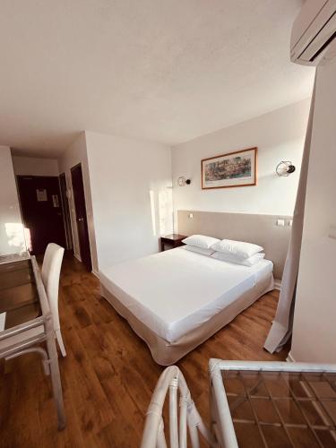 a bedroom with a white bed and a wooden floor at Tropic Hôtel in Rivesaltes