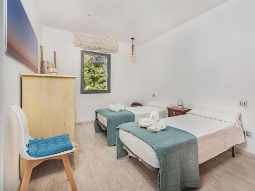 a bedroom with two beds and a chair and a window at Playa de Muro Chalet with Pool for 6 in Playa de Muro