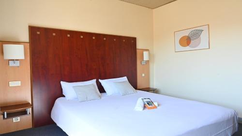 a bedroom with a large white bed with a wooden headboard at Logis Hôtel & Restaurant Le Cheval Blanc et Clovis in Vouillé