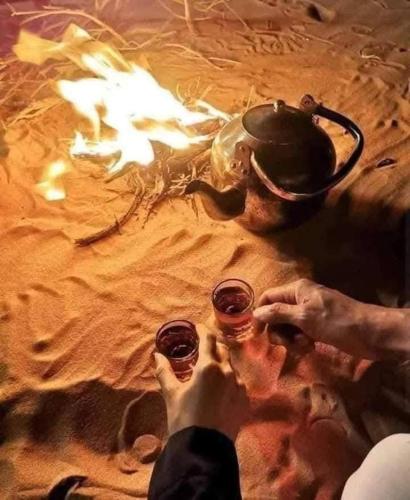 two people are holding wine glasses in front of a fire at Fayoum Safari Camp in Qaryat at Ta‘mīr as Siyāḩīyah
