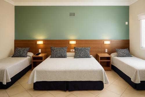 a hotel room with two beds and two tables at Hotel Nova York in Araçatuba