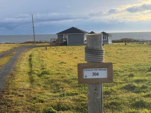 a sign on a pole in a field with a house at Waterfront & breathtaking view - Chalet du Phare in Bonaventure