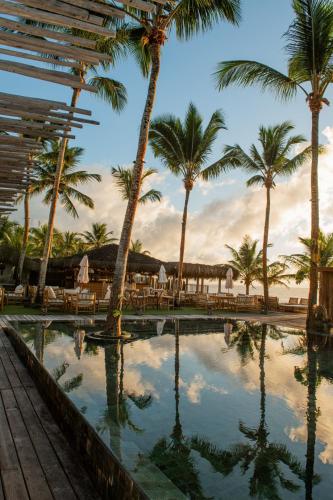 a resort swimming pool with palm trees and chairs at Pousada Vila do Mar in Caraíva